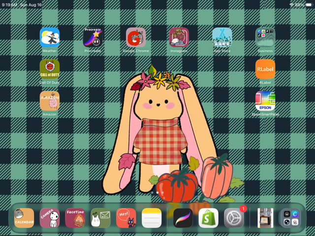 An iPad home screen displaying a custom digital wallpaper with a green and black plaid pattern and a central cartoon bunny wearing a red plaid dress and autumn leaf crown, surrounded by various app icons.