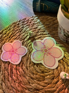 Two pink and white rainbow holographic cherry blossom sakura flower stickers or decals displayed on a woven straw mat.