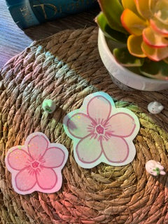 Two pink and white rainbow holographic cherry blossom sakura flower stickers or decals displayed on a woven straw mat.