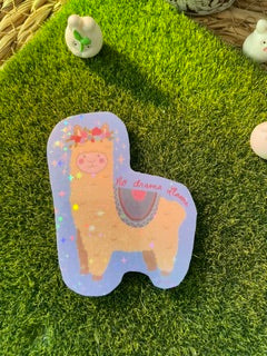 A small irregular-shaped translucent lavender item with a printed tan animal illustration and tiny colorful flecks, placed on artificial green grass with small decorative stones nearby.